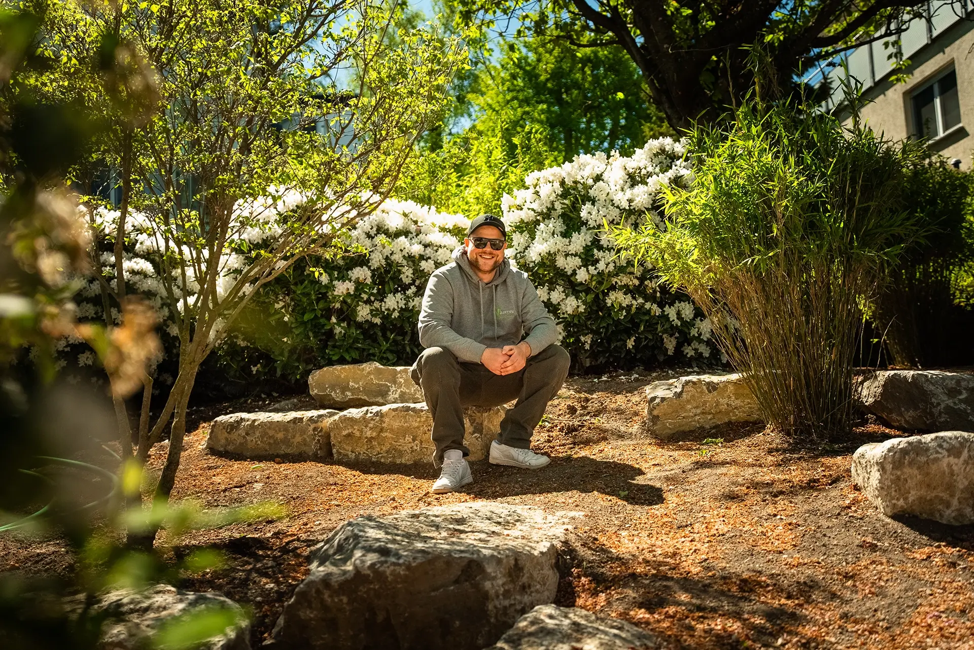 Leon Martin, Inhaber, in einem von ihm gestalteten Garten mit Natursteinen und blühenden Rhododendren